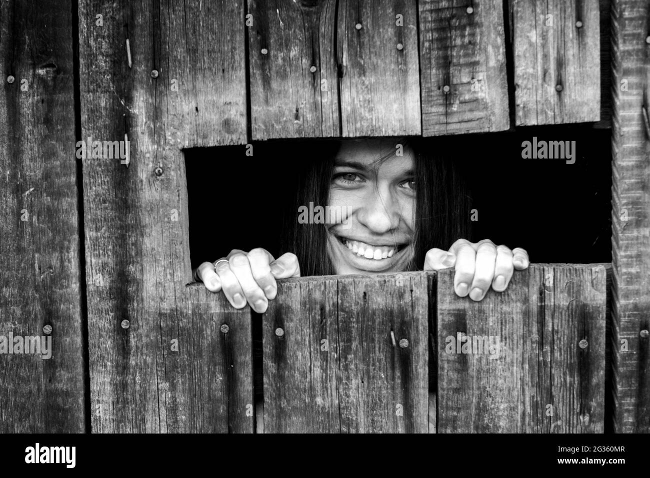 Une jeune femme qui pase à travers une petite fenêtre. Photo en noir et blanc. Banque D'Images