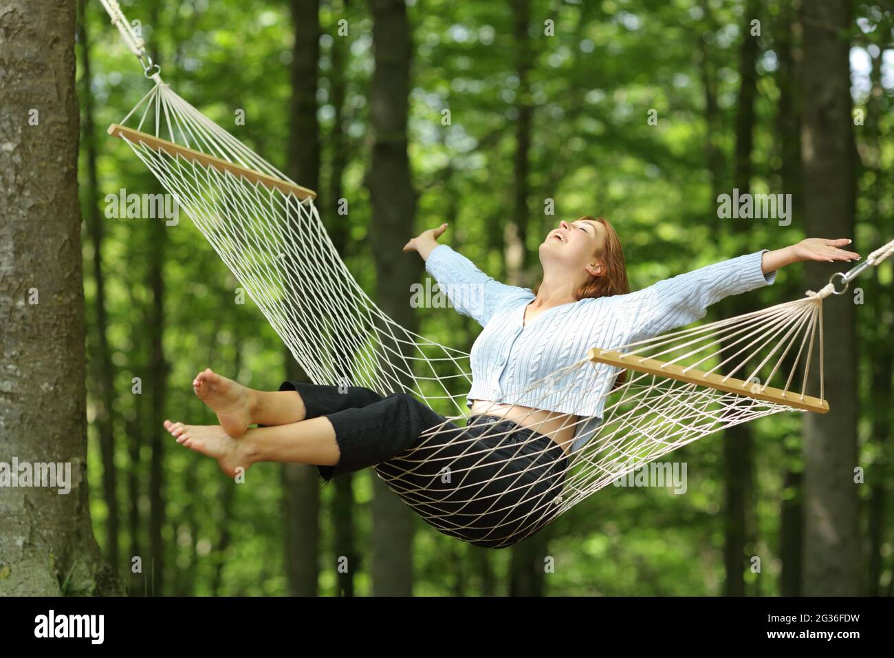 Une femme heureuse se balançant sur un hamac dépassant les bras dans une forêt Banque D'Images