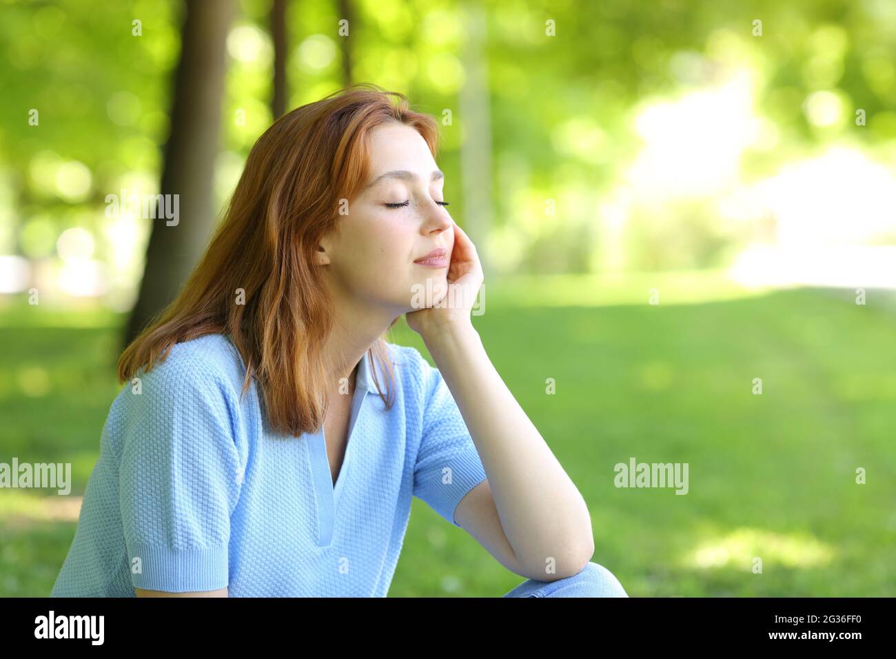 Femme décontractée assise dans un parc aux yeux fermés Banque D'Images