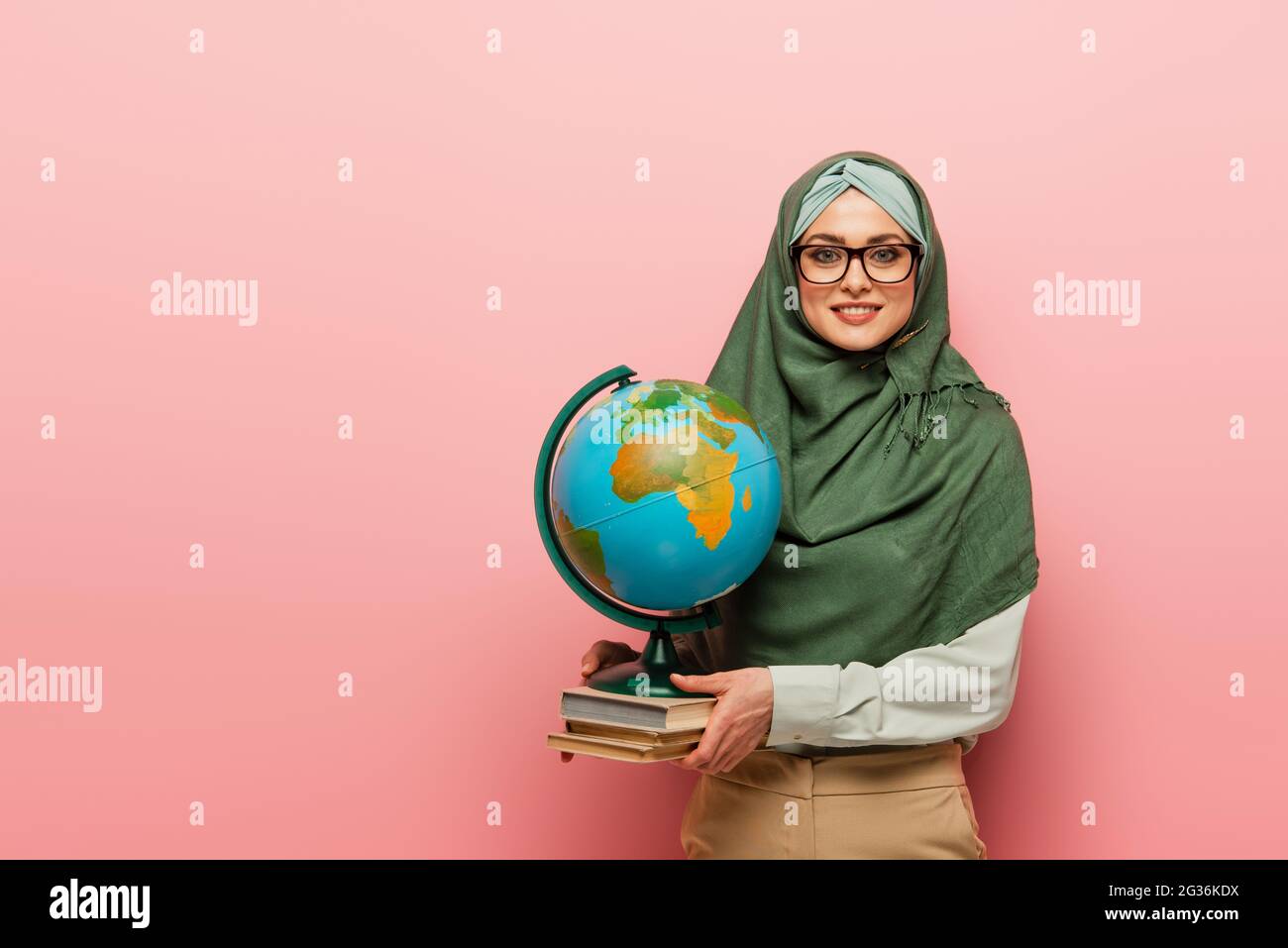 professeur musulman souriant avec des manuels scolaires et un globe regardant l'appareil photo sur fond rose Banque D'Images