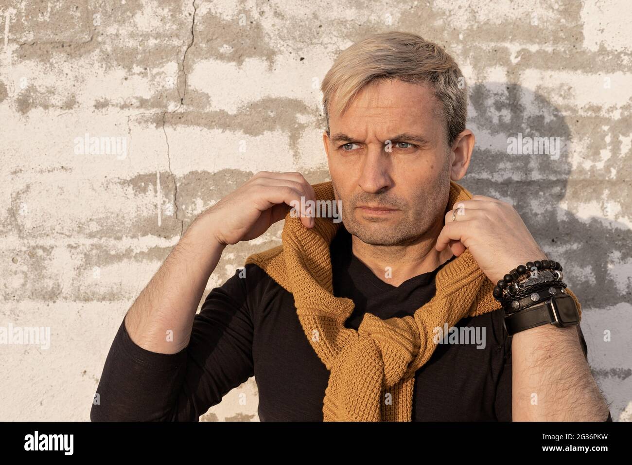 Charmant et élégant blond d'âge moyen homme caucasien d'apparence modèle devant un mur de briques blanches. Beau modèle élégant et élégant pour homme mature dans une ambiance décontractée Banque D'Images