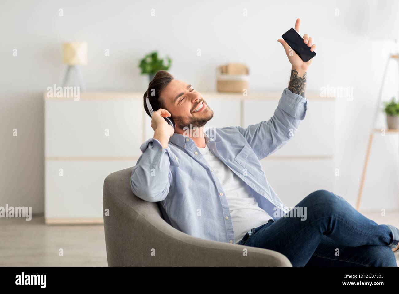 Bonne pause. Un homme positif avec un smartphone et un casque qui écoute de la musique à la maison, en appréciant sa chanson préférée Banque D'Images