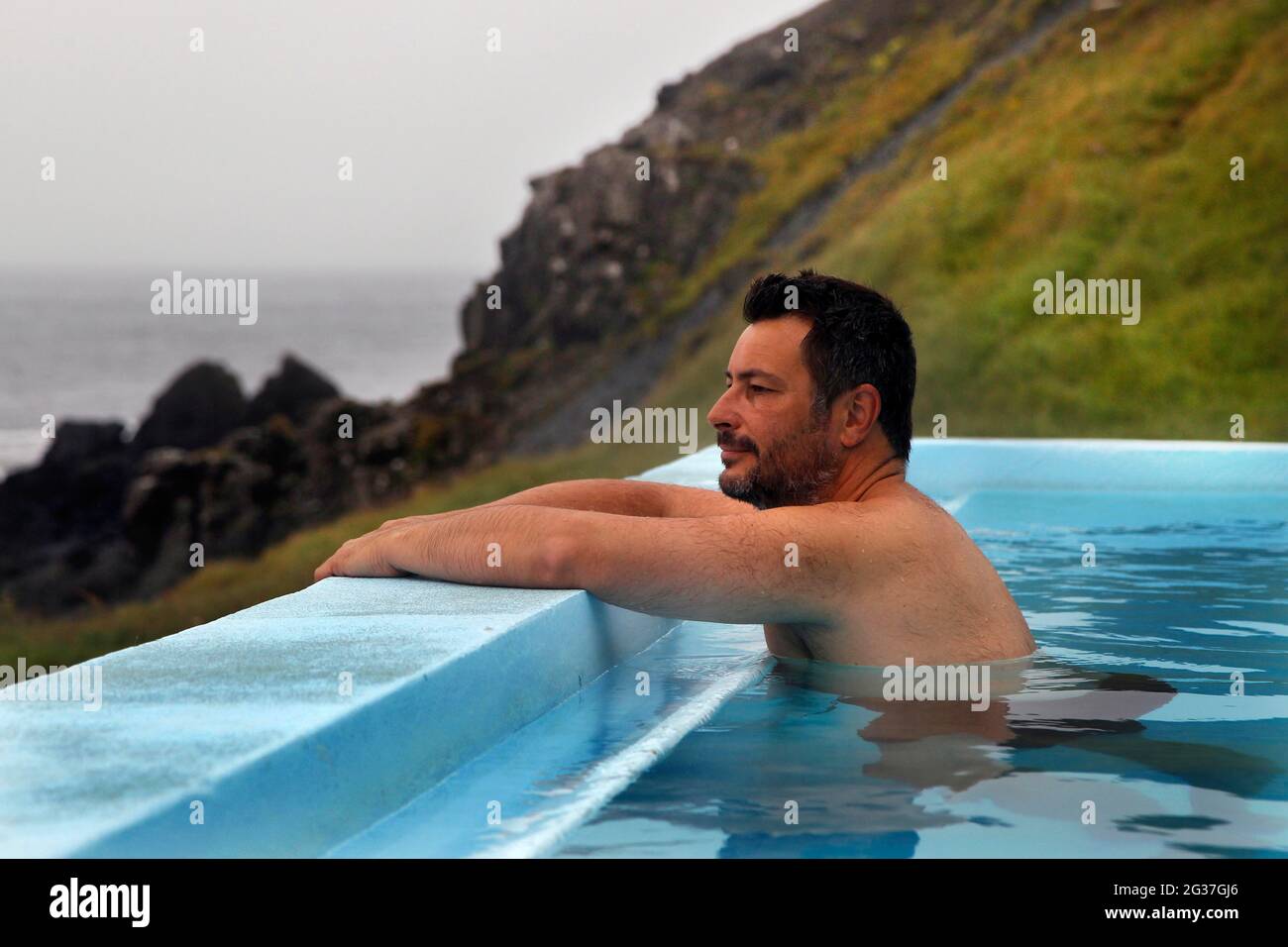 Homme dans la piscine, piscine extérieure avec vue sur l'océan Atlantique, Norourfjoerour, Vestfiroir, Westfjords, Nord-Ouest de l'Islande, Islande Banque D'Images