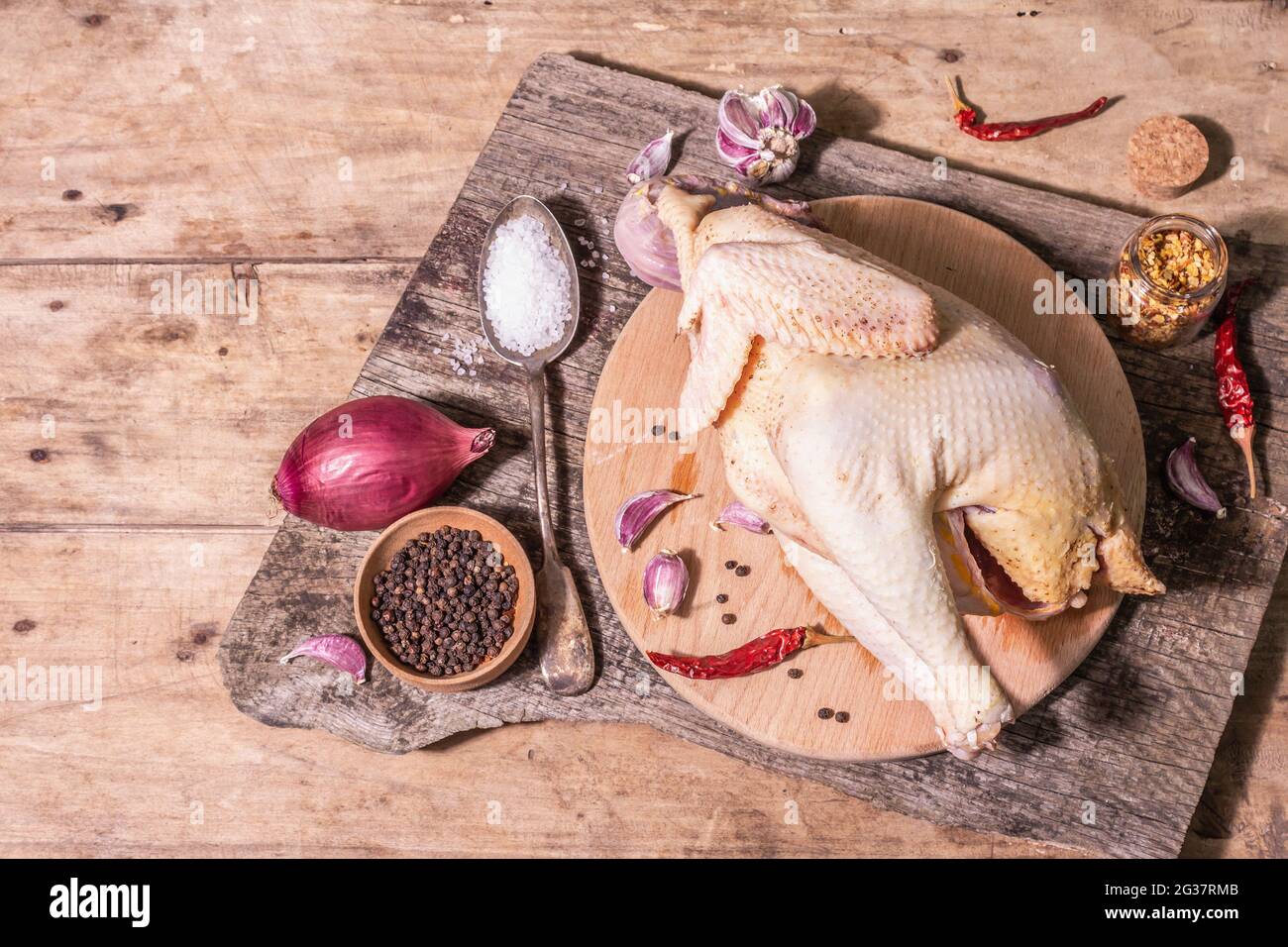 Carcasse brute de poulet entier pour un mode de vie alimentaire sain. Oiseau de ferme à aire libre avec oignon rouge, gousses d'ail, épices et sel de mer. Une lumière dure tendance, d Banque D'Images