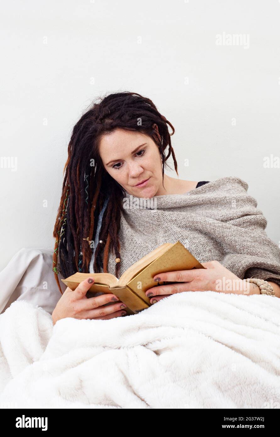 femme se détendant à la maison, confortable dans une couverture, lecture Banque D'Images