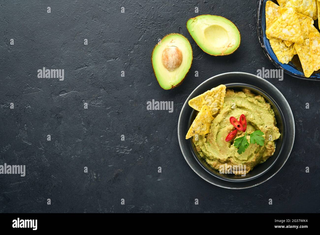 Guacamole. Sauce mexicaine traditionnelle latinaméricaine dans un bol noir avec avocat et ingrédients et nachos de maïs. Propagation de l'avocat. Vue de dessus. Copyspa Banque D'Images