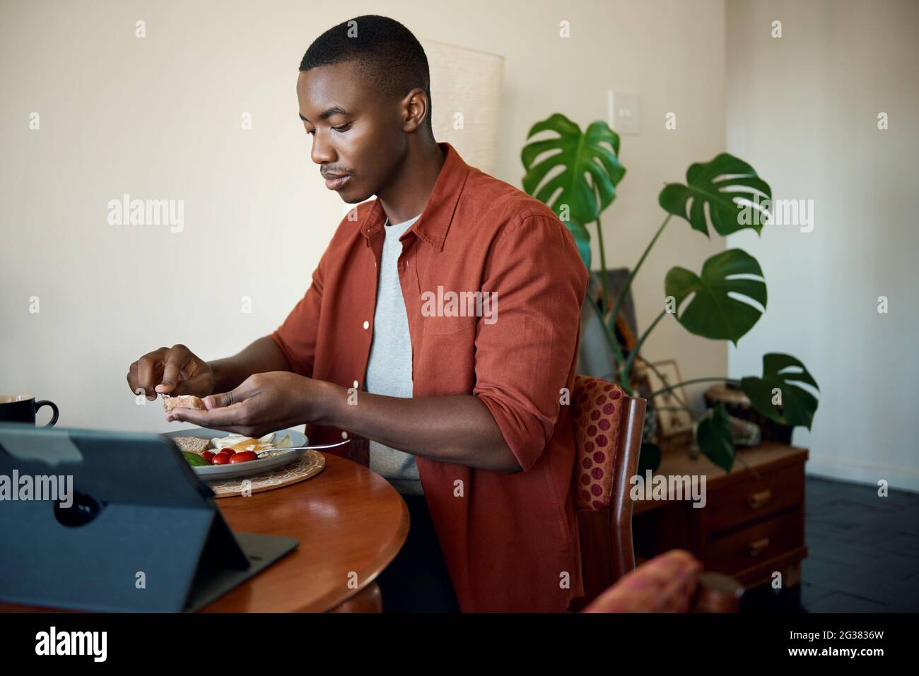 Jeune homme africain prenant le petit déjeuner et utilisant une tablette numérique Banque D'Images