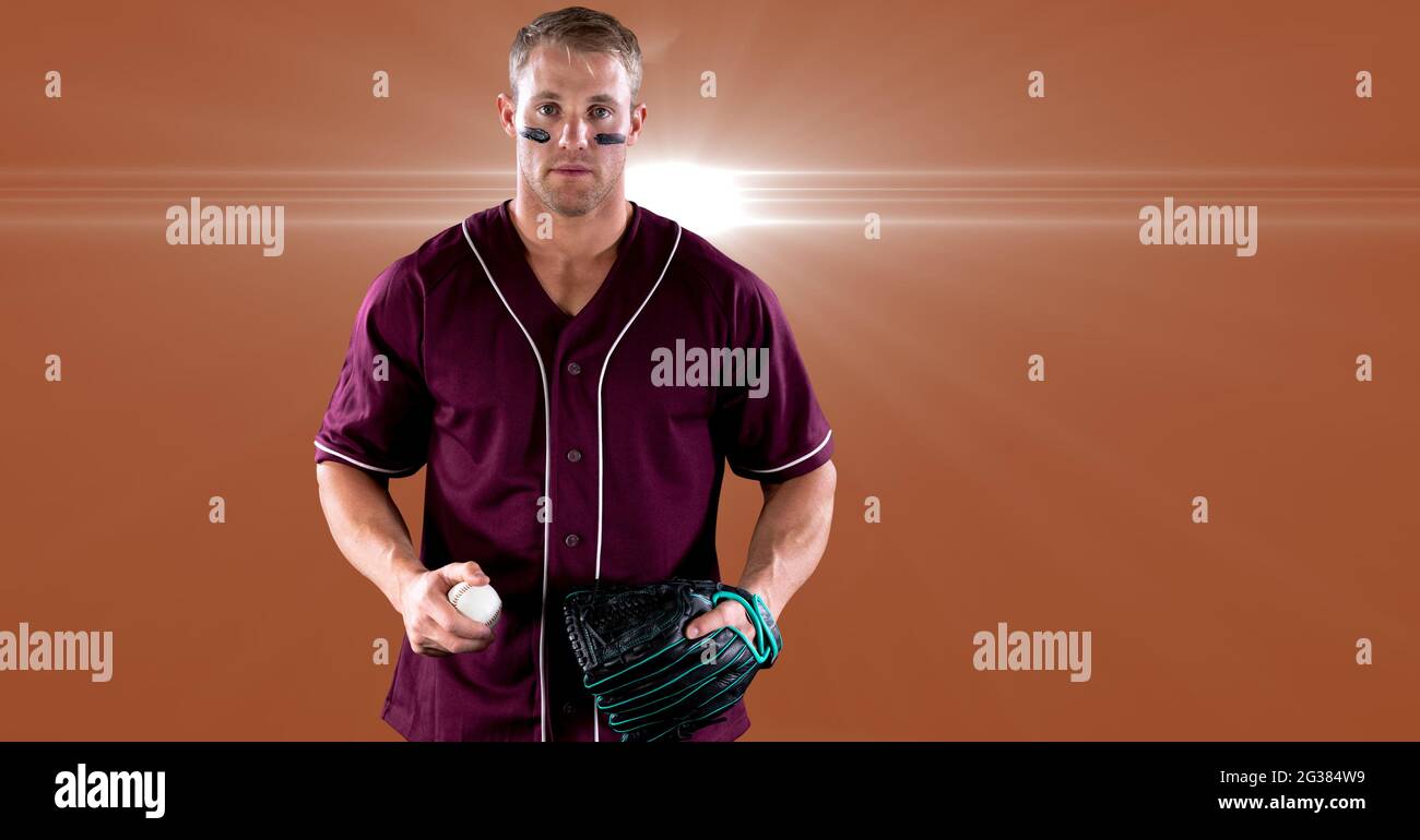 Portrait du pichet de baseball mâle caucasien tenant la balle contre la tache de lumière sur fond orange Banque D'Images