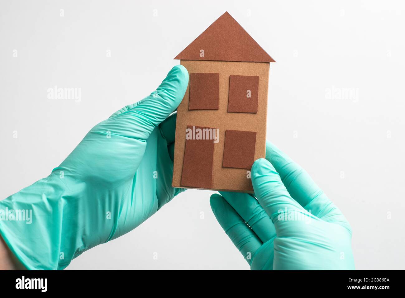 Mains en gants tenant une maison en papier sur fond blanc Banque D'Images