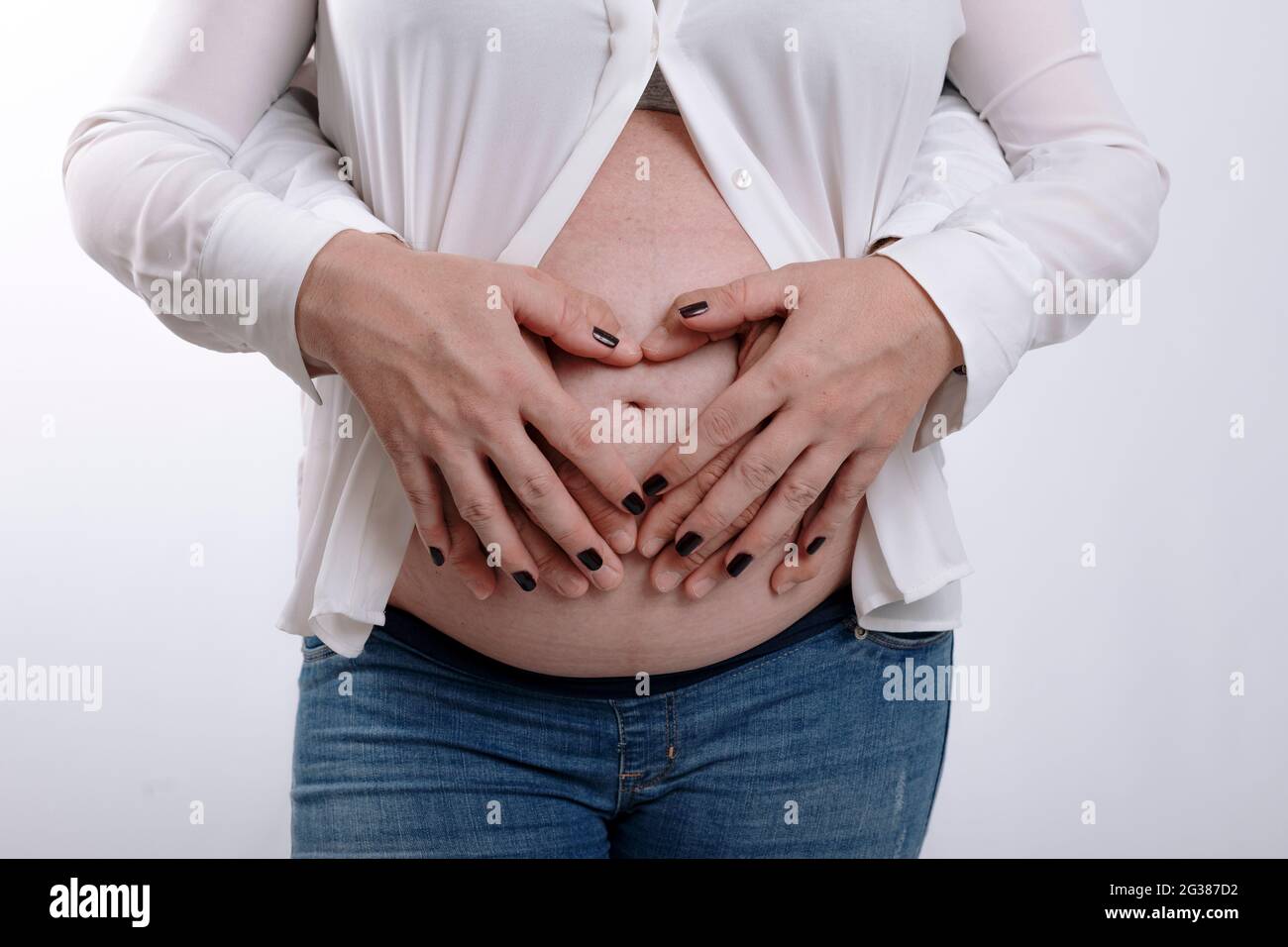 Femme enceinte et son mari tenant les mains sur le ventre. Couple s'attendant à un bébé en studio avec fond blanc Banque D'Images