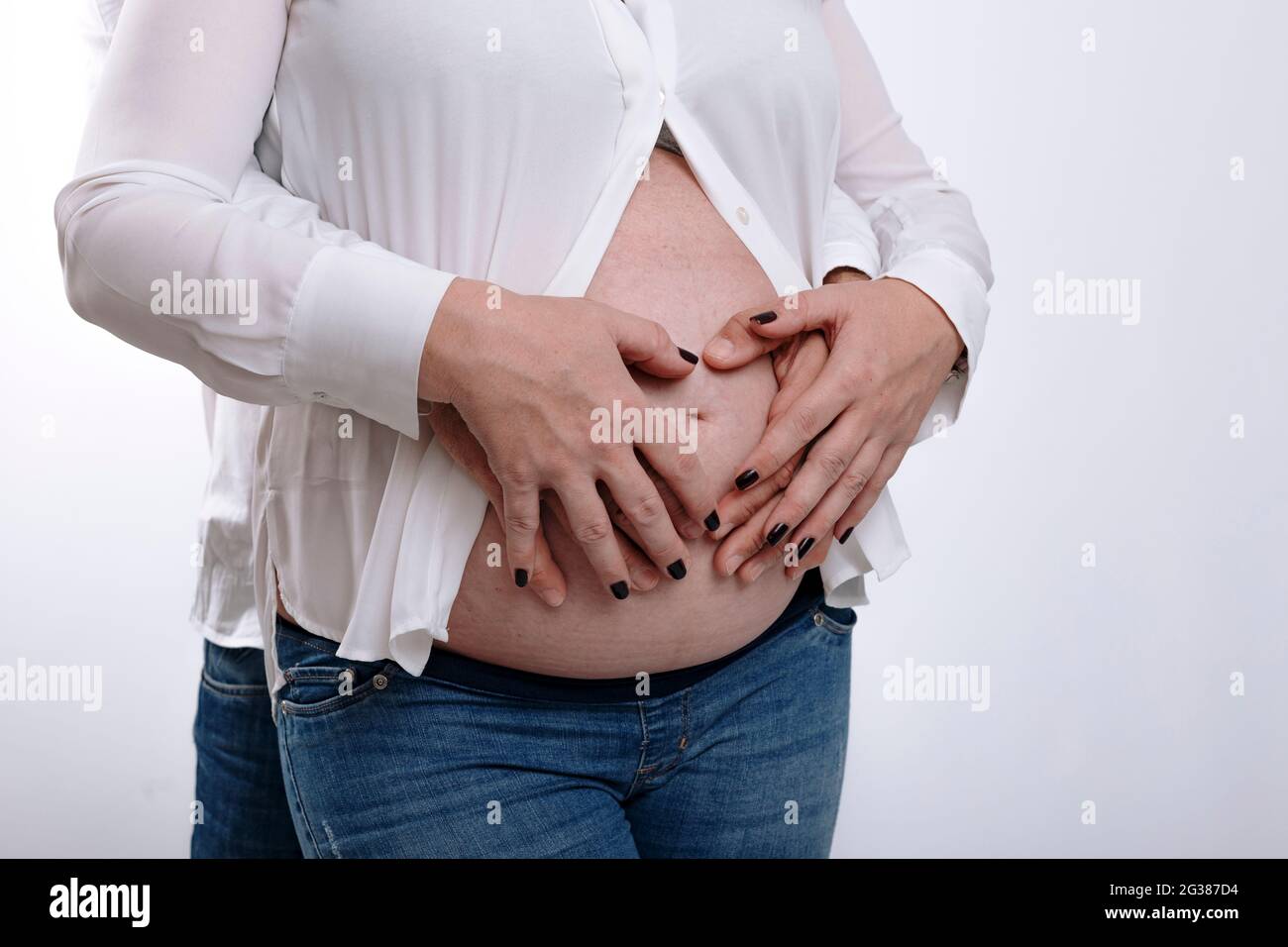 Femme enceinte et son mari tenant les mains sur le ventre. Couple s'attendant à un bébé en studio avec fond blanc Banque D'Images