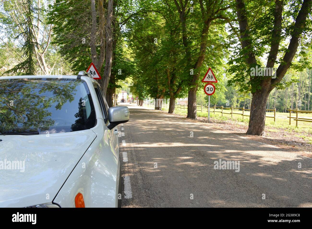 4x4 blanc stationné au bord de la route d'entrée du village de Yanguas, à Soria. Indicateur de vitesse à 30km h et arbres sur les côtés de la route. Banque D'Images
