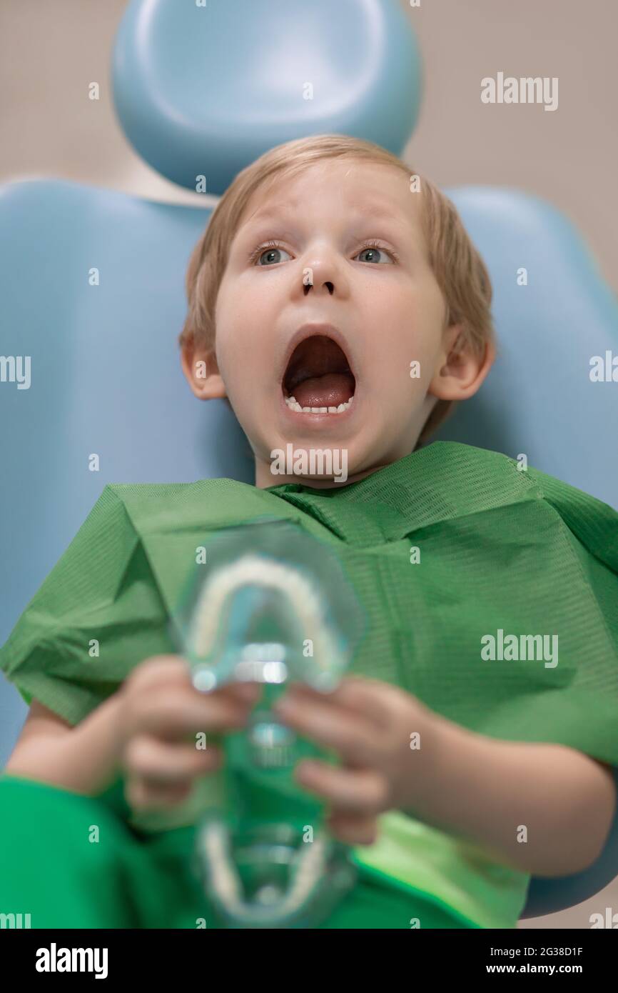 Un enfant avec sa bouche très ouverte attend un examen de médecin en chaise dentaire chez le dentiste. Concept de dentisterie et d'hygiène dentaire pour bébés. Banque D'Images