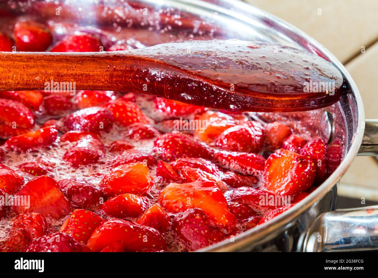 Faire de la confiture de fraises à la maison - cuillère en bois sur le bord de la casserole en acier inoxydable. Étape 4 sur 4. Banque D'Images