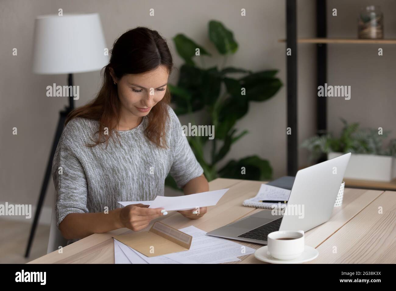 Une femme satisfaite lisant les bonnes nouvelles dans la lettre, assise à son bureau Banque D'Images