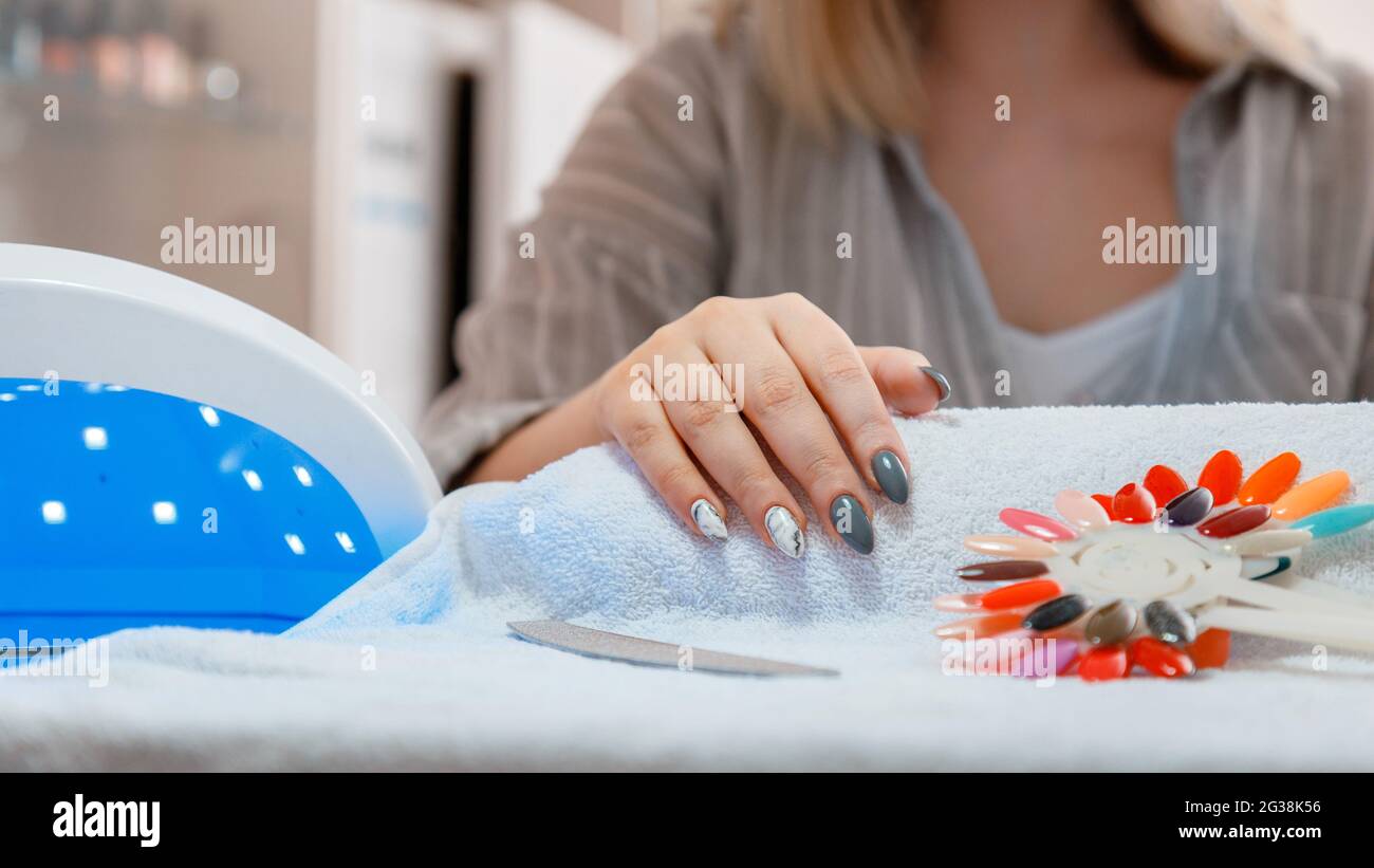 Femme avec des ongles acryliques artificiels ramasse une nouvelle couleur de polissage lors de la procédure de manucure. Manucure dans le salon de beauté. Hygiène beauté des mains dedans Banque D'Images