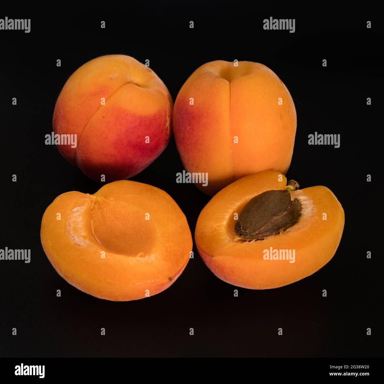 Un bouquet de fruits abricot mûrs, deux parties entières et deux parties séparées, sur un fond noir isolé Banque D'Images