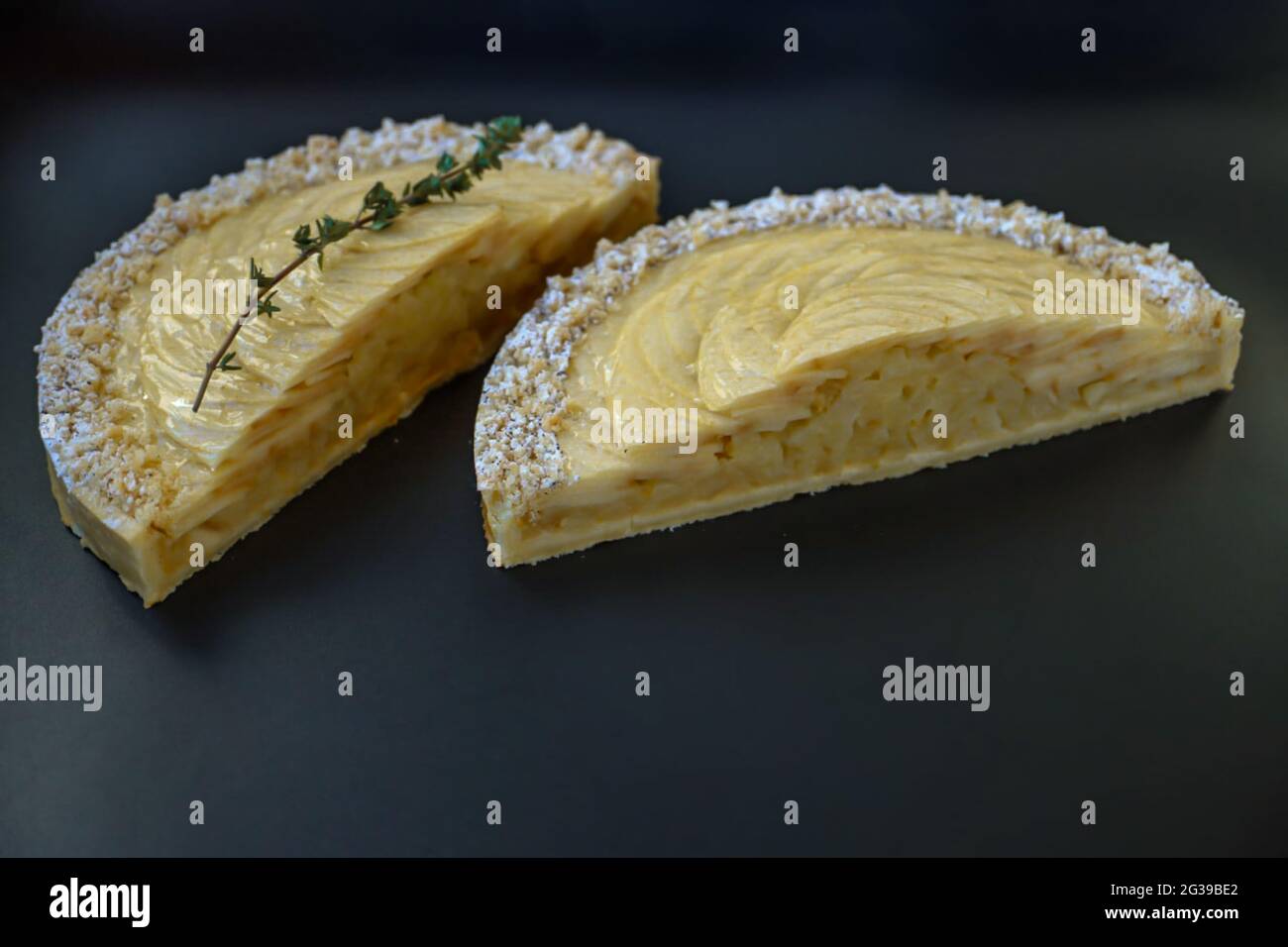 Tarte aux pommes coupée en deux avec branche de thym vert sur police noire Banque D'Images