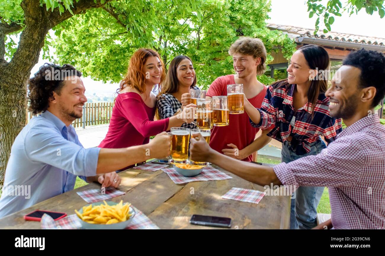 groupe multiéthique de personnes appréciant la bière ensemble en plein air assis sur une table de jardin. divers heureux amis ayant le plaisir de faire un toast boire de l'alcool Banque D'Images