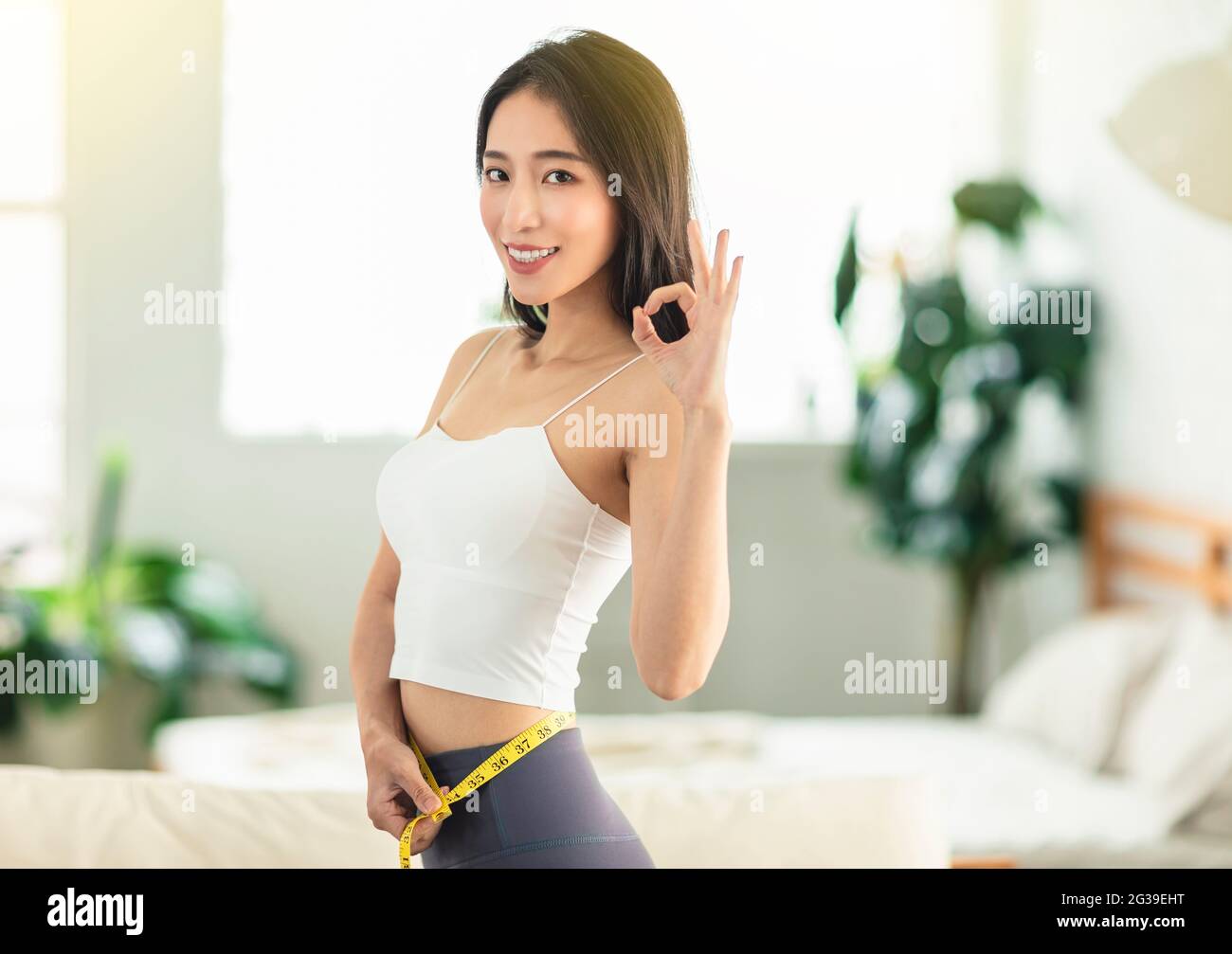 Jeune femme tenant une règle de mesure tout en dansant, tournant autour, très satisfait de sa posture, très heureux de perdre du poids, avec un geste OK Banque D'Images