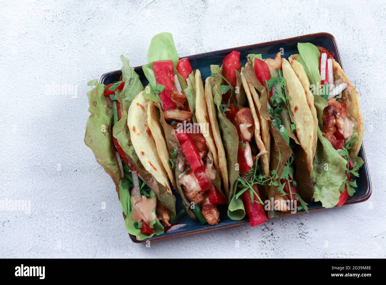 Tacos avec salade verte, poivre, poulet sur une assiette carrée sur fond gris clair. Vue de dessus, plan d'appartement Banque D'Images