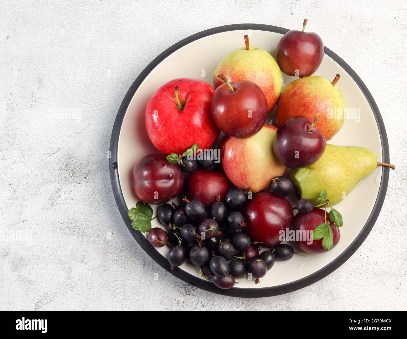 Fruits crus - pommes, poires, prunes et groseilles sur une assiette ronde sur fond gris clair. Vue de dessus, plan d'appartement Banque D'Images