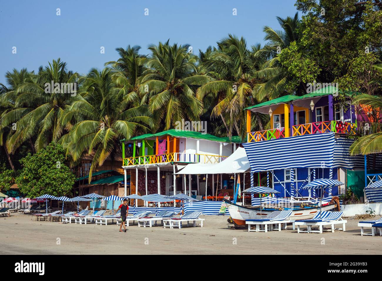 Chaises longues et huttes de plage colorées sous de jolis palmiers et ciel bleu, Palolem, Goa, Inde Banque D'Images