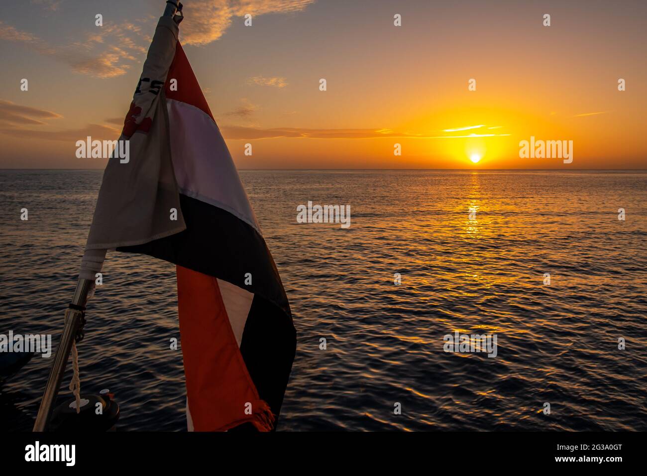 Drapeau de l'Égypte agitant sur un navire avec beau coucher de soleil orange et violet sur la mer Rouge en arrière-plan. Banque D'Images