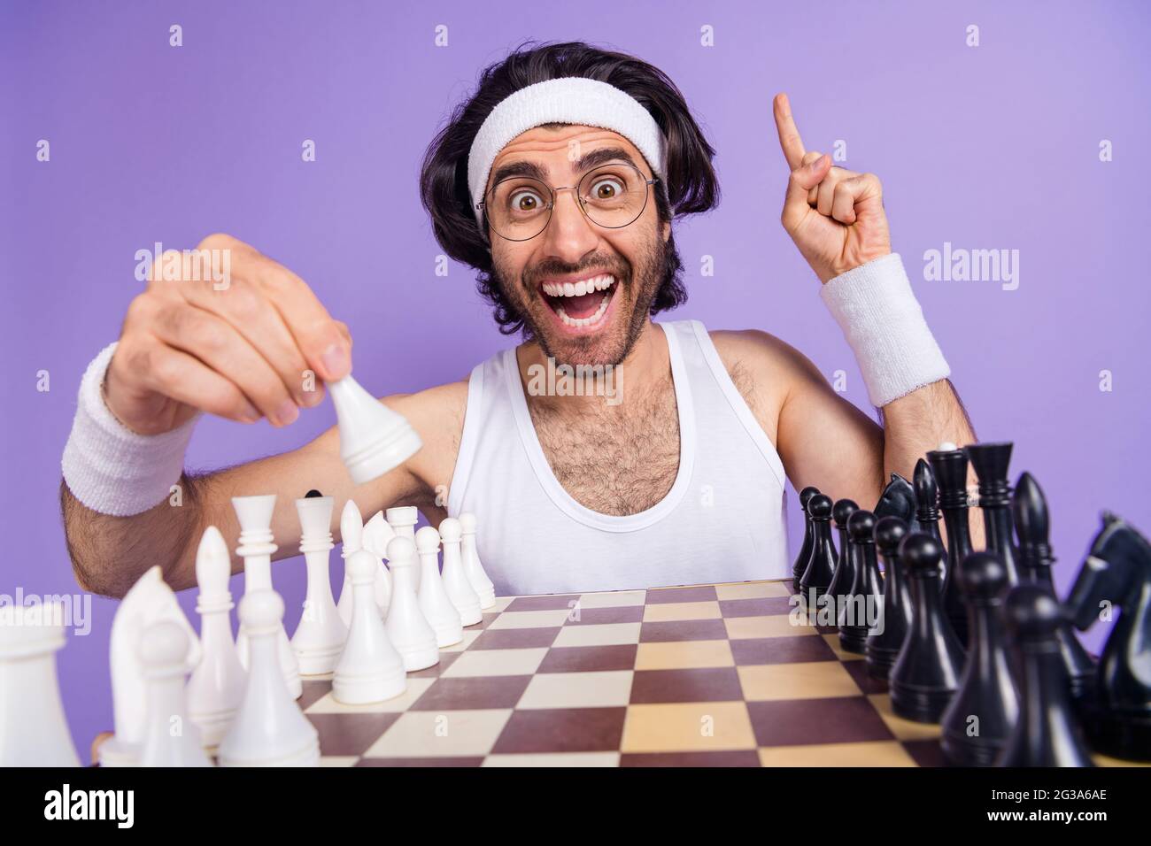Photo de brunette optimiste gars jouer échecs porter des lunettes blanc singlet hairband isolé sur fond de couleur lilas Banque D'Images
