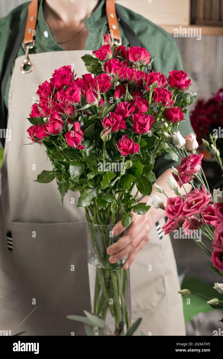 Une femme fleuriste dans un tablier tient un vase de roses. Les gens au travail. Lieu de travail du fleuriste. Fleuriste. Concept de petite entreprise. Gros plan. Tir vertical Banque D'Images