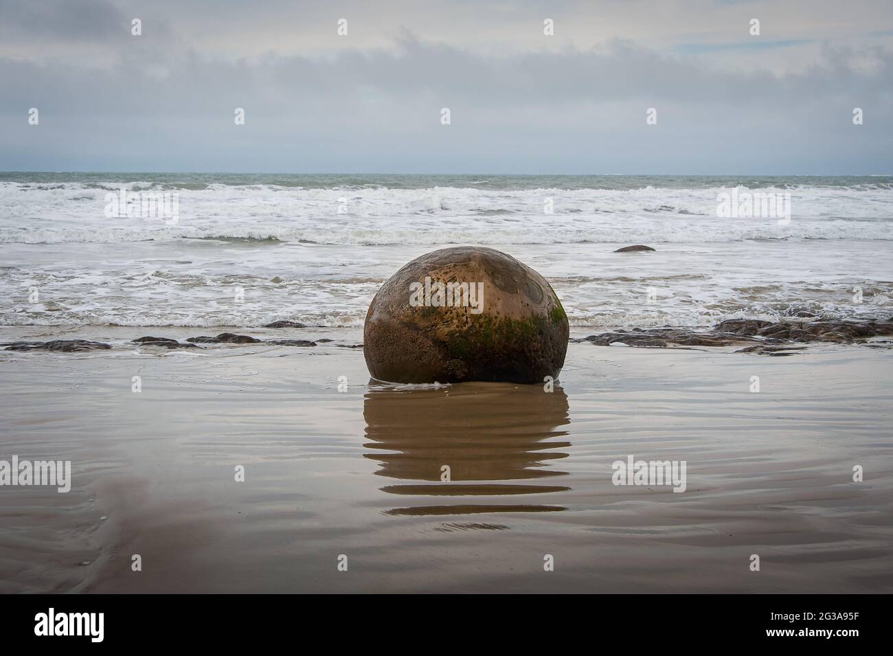 Les Moeraki Boulders sur la plage de Koekohe, Otago. Un seul rocher et des réflexions avec fond gris mer/ciel Banque D'Images