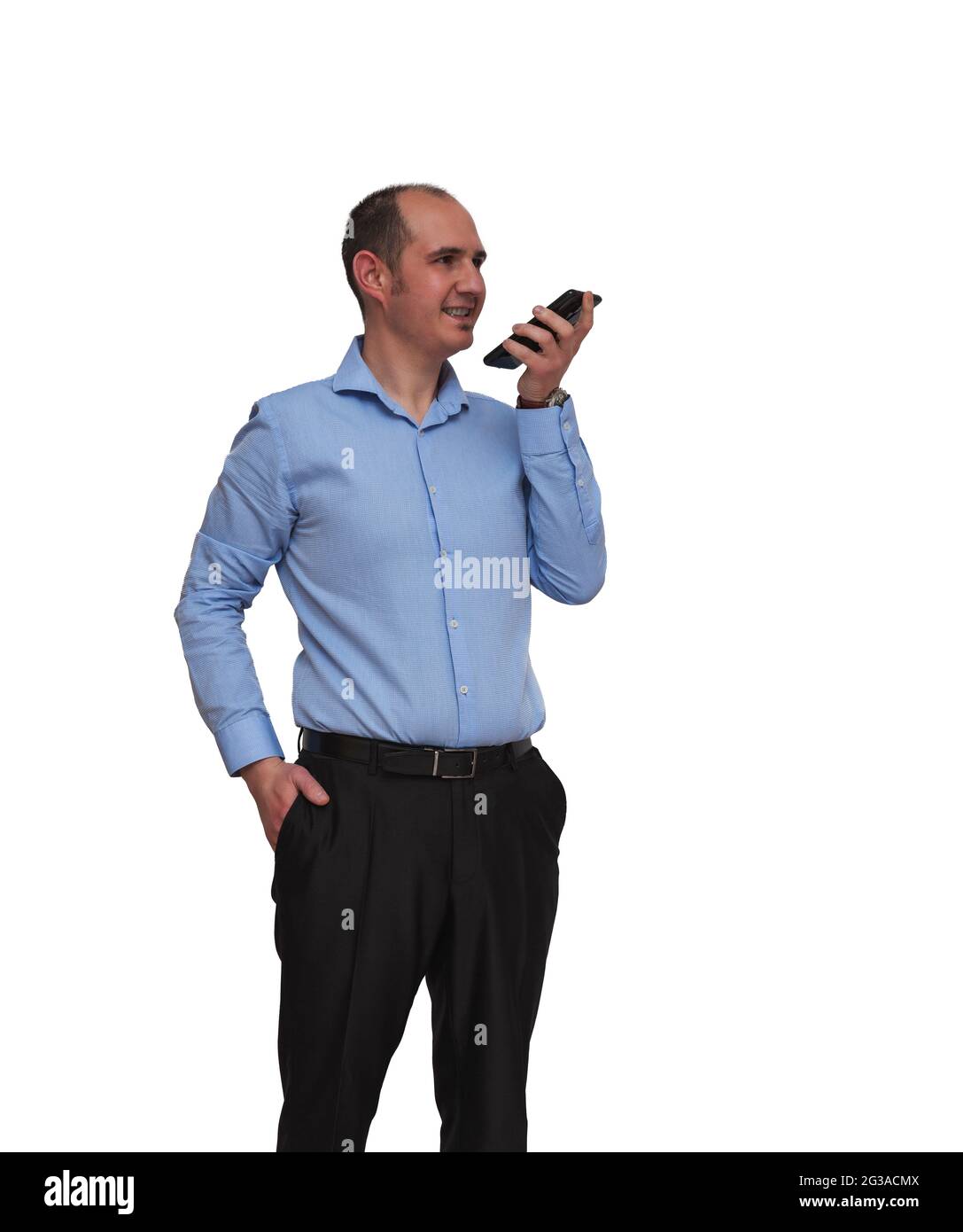 Un homme chauve habillé d'une chemise bleue et d'un pantalon noir  enregistrant un message audio avec son smartphone isolé sur fond blanc.  Peut être un employé de bureau ou ba Photo Stock -