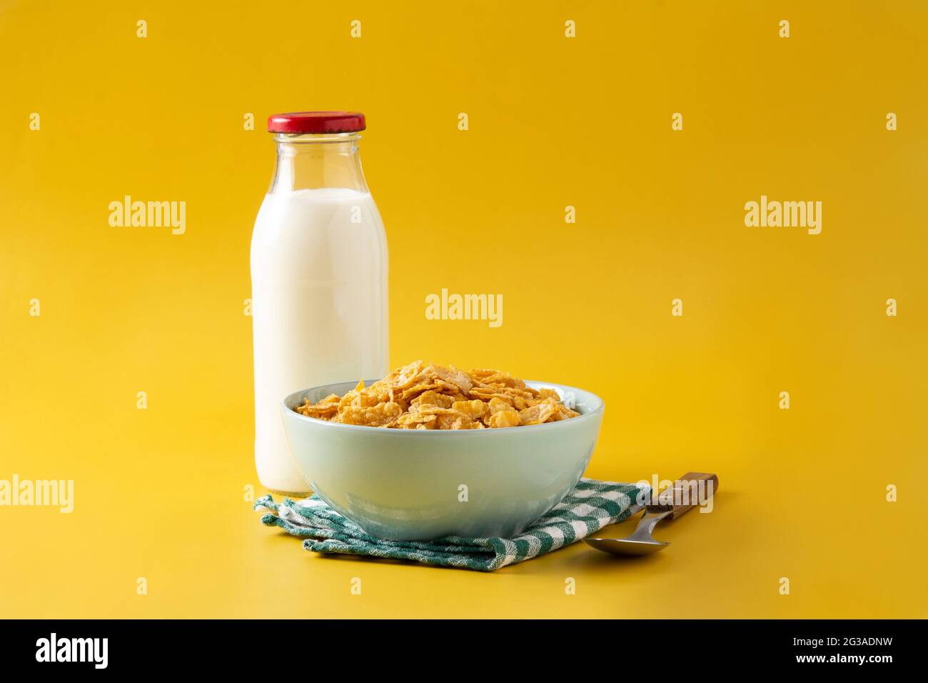 Flocons de maïs dans un bol bleu et bouteille de lait sur fond jaune Banque D'Images