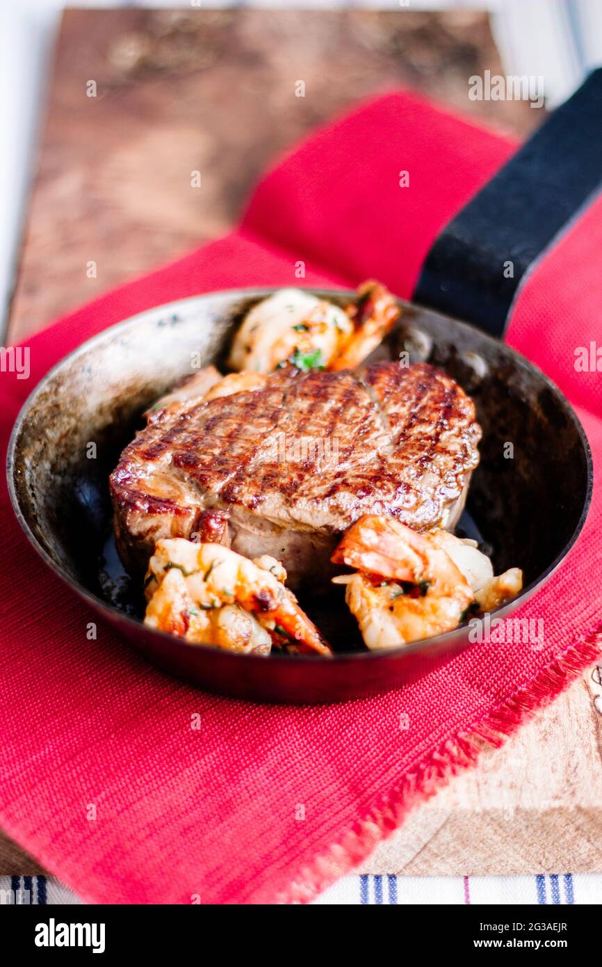 Steak de filet dans une poêle à frire avec des marques de griddle et des crevettes, Surf n Turf, sur une planche à bois, serviette de table rouge rustique Banque D'Images