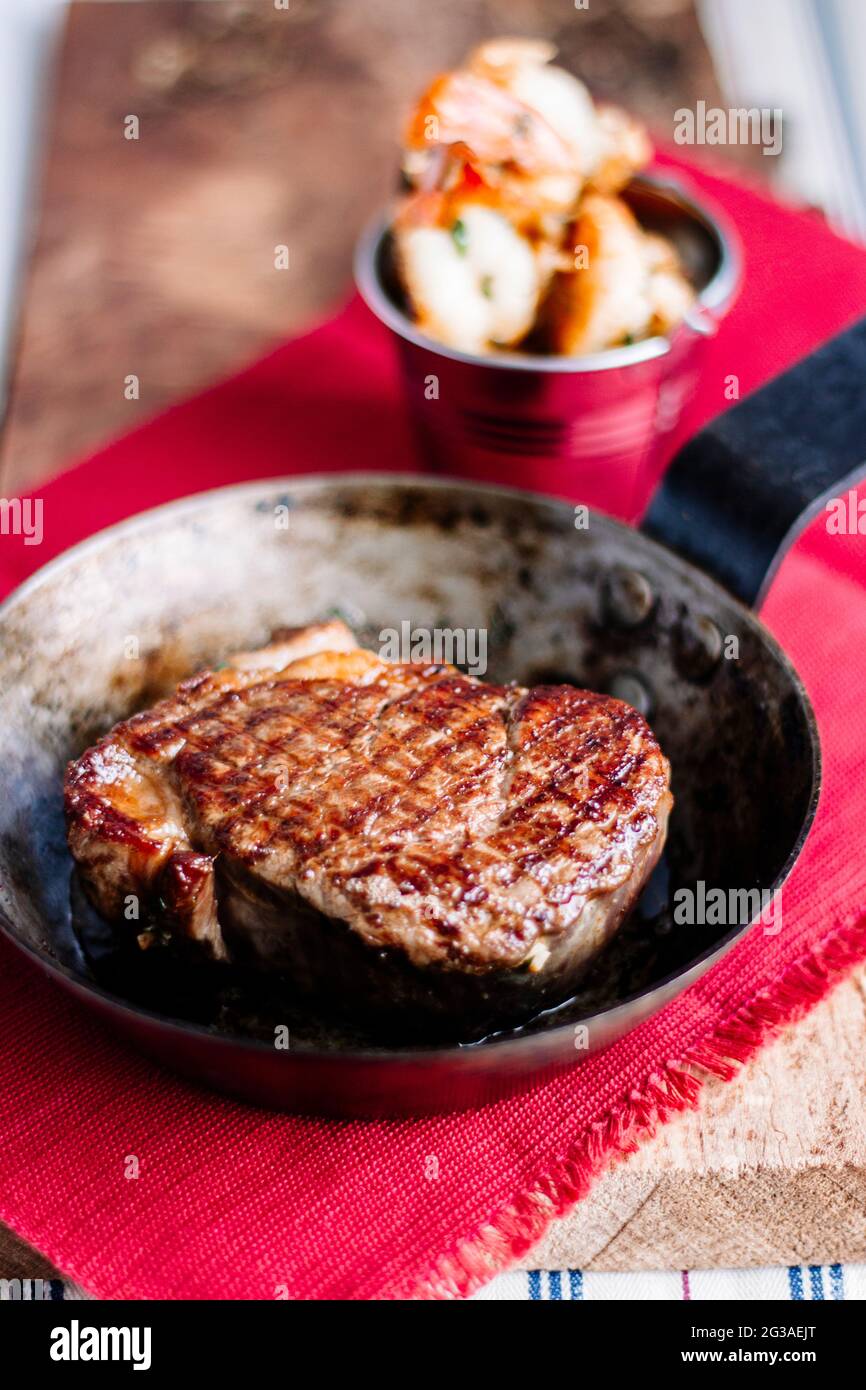 Steak de filet dans une poêle à frire avec des marques de griddle et des crevettes, Surf n Turf, sur une planche à bois, serviette de table rouge rustique Banque D'Images