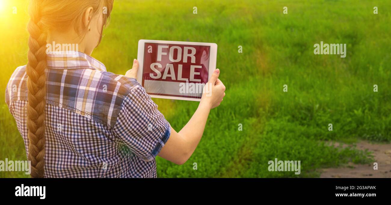 Fille tient tablette avec pour la vente texte, fond de champ vert, parcelle de terrain pour la construction de maison, bannière Banque D'Images
