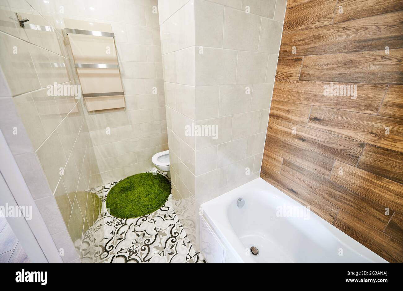 Vue sur la partie gauche de la petite salle de bains lumineuse avec rénovation moderne. Carreaux blancs sur les murs se combinant avec des éléments en bois, plomberie en céramique et tapis de bain vert. Banque D'Images