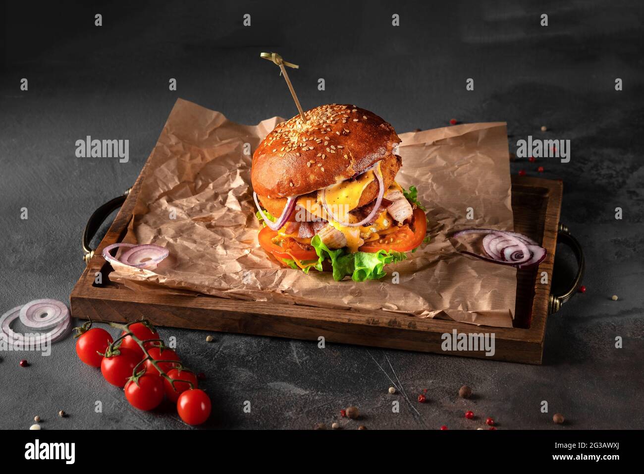 grand hamburger américain sur fond noir. côtelette avec fromage, tomate et champignons sur un plateau en bois, vue latérale Banque D'Images
