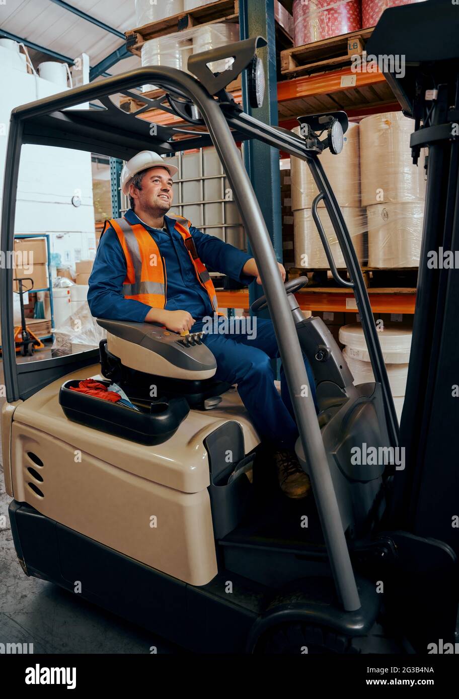 Portrait d'un ouvrier d'entrepôt heureux assis dans un chariot élévateur dans un grand entrepôt Banque D'Images