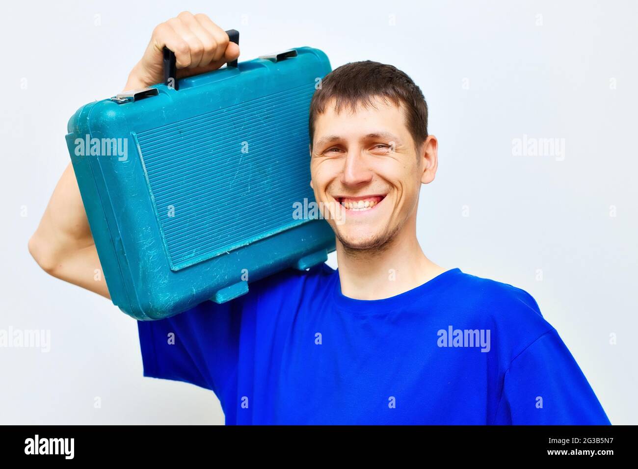 Portrait d'un serrurier positif large sourire. Un travailleur porte une mallette à outils sur son épaule. Un réparateur. Banque D'Images
