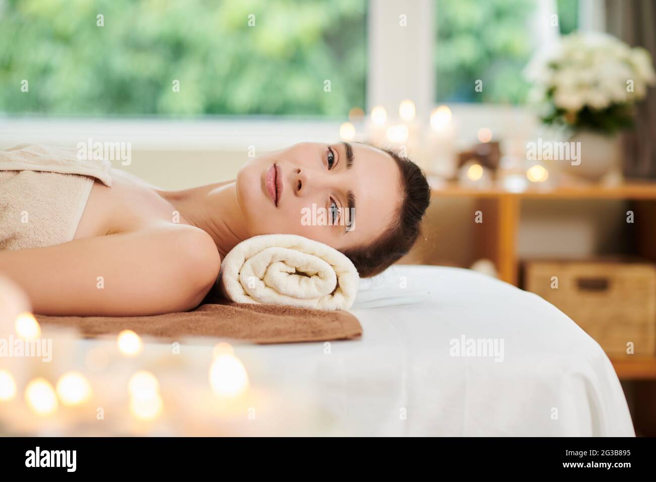 Portrait d'une jeune femme regardant l'appareil photo tout en se reposant sur un lit dans un salon de spa Banque D'Images