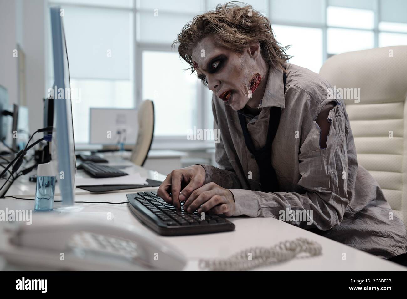 Un homme laid avec un maquillage zombie travaillant avec un ordinateur au bureau Banque D'Images