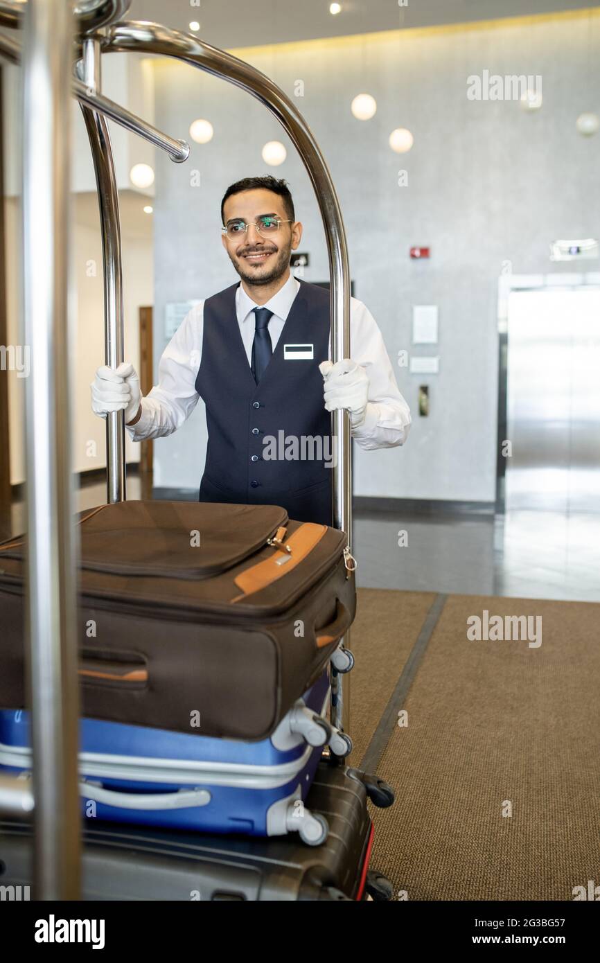 Un jeune porteur d'hôtel dans un chariot de transport uniforme avec bagages de voyageurs Banque D'Images