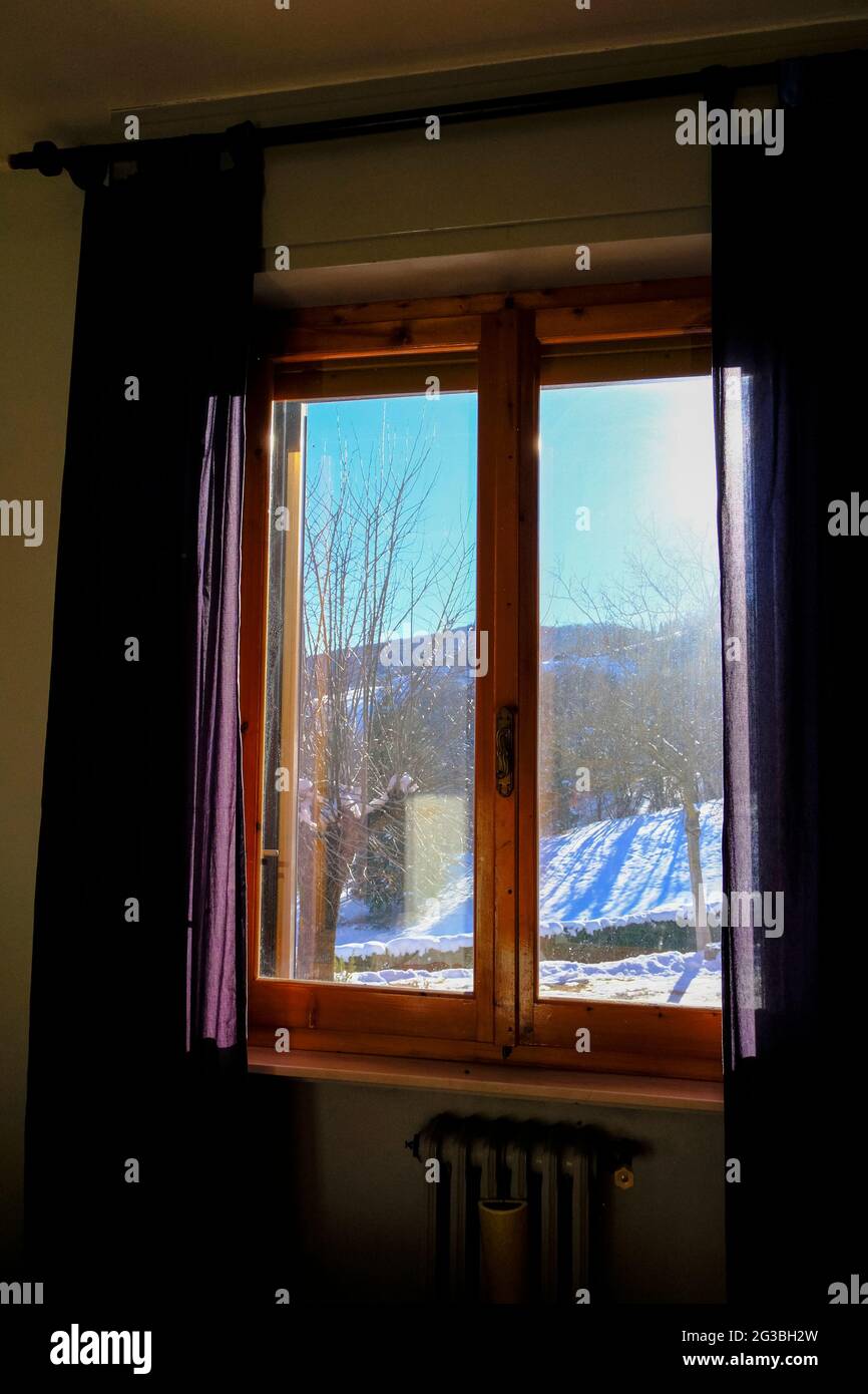 Vue d'hiver par temps ensoleillé depuis la fenêtre en bois avec rideaux bleus. Intérieur de la maison. Conception de fenêtres Banque D'Images