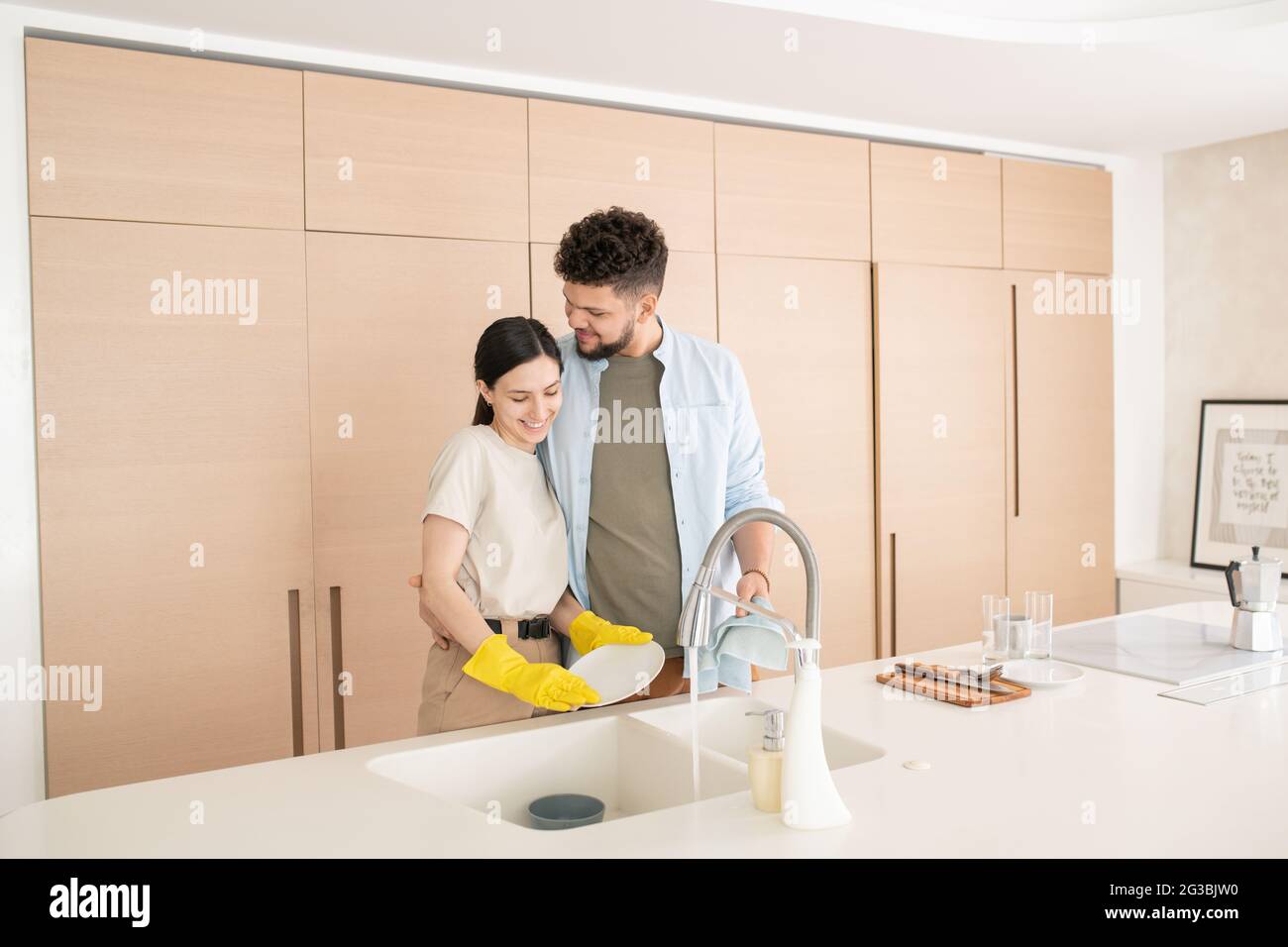 Un homme heureux embrassant sa femme en lavant les plats après le petit déjeuner Banque D'Images