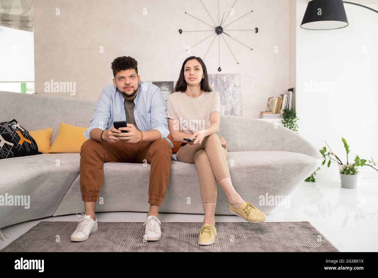 Jeune couple contemporain assis sur un canapé et regardant la télévision dans la salle de séjour Banque D'Images