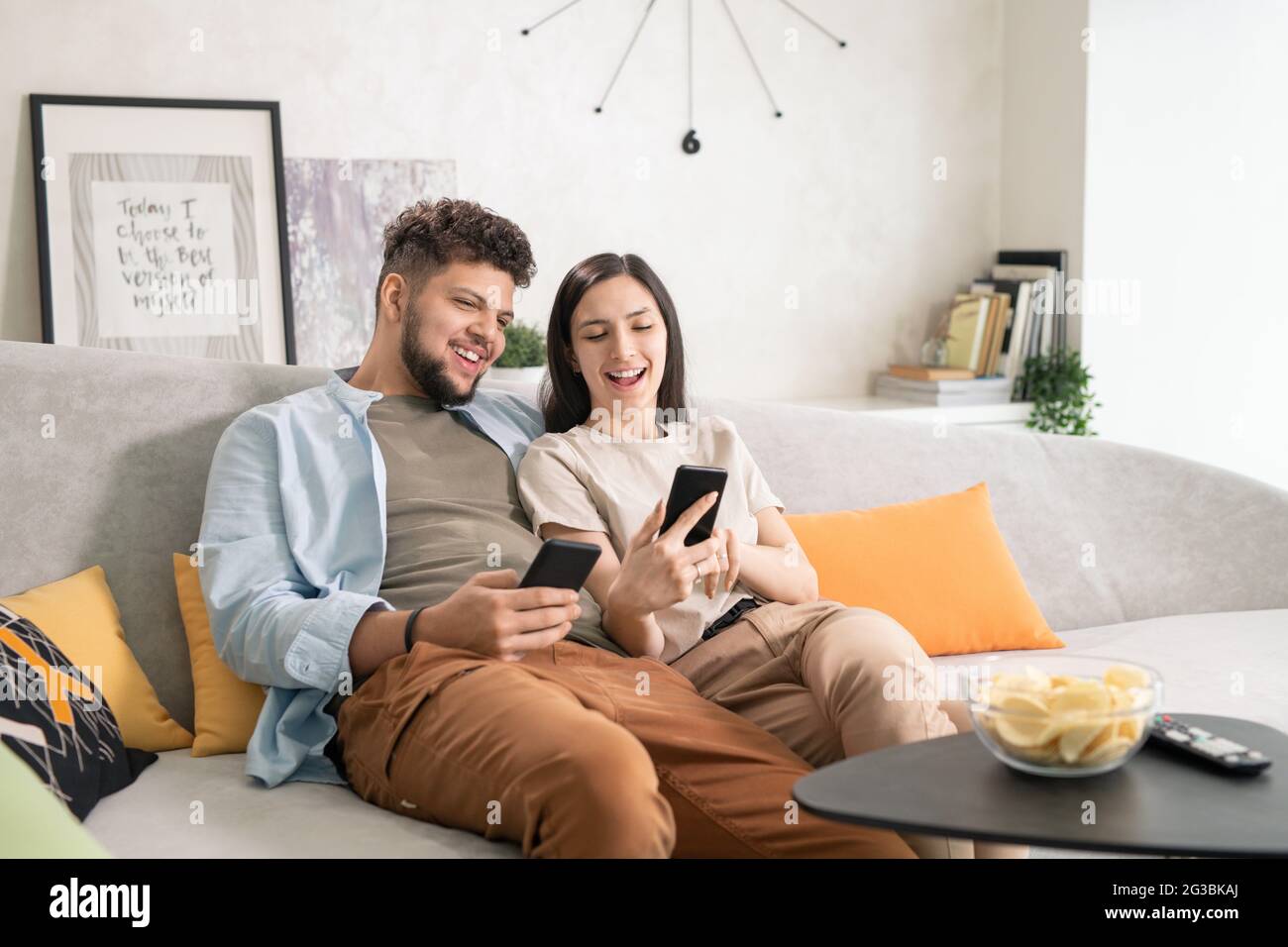 Couple joyeux utilisant un smartphone tout en se reposant sur un canapé dans le salon Banque D'Images