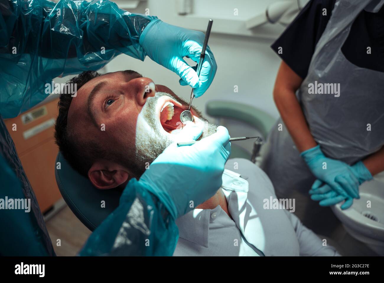 Mâle caucasien assis avec la bouche large ouverte tandis que le dentiste mâle nettoie les dents Banque D'Images