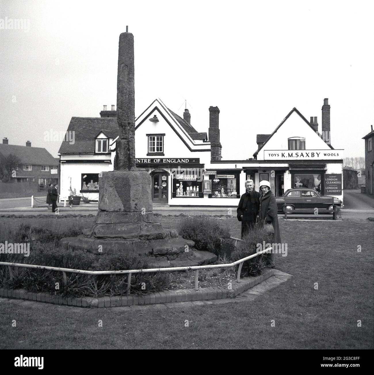 1950s, historique, deux dames debout près d'une vieille pierre commémorative dans un village vert, Angleterre, Royaume-Uni. Un MAGASIN DE ESPAR derrière eux dit "Centre de l'Angleterre". Le premier magasin SPAR en Grande-Bretagne a été établi au milieu des années 50 et, à mesure qu'il s'est agrandi, est devenu connu pour leur quartier, les dépanneurs locaux. A côté de LA SPAR se trouve un magasin, K. M Saxby, un vendeur de fleurs et de Wools. Banque D'Images