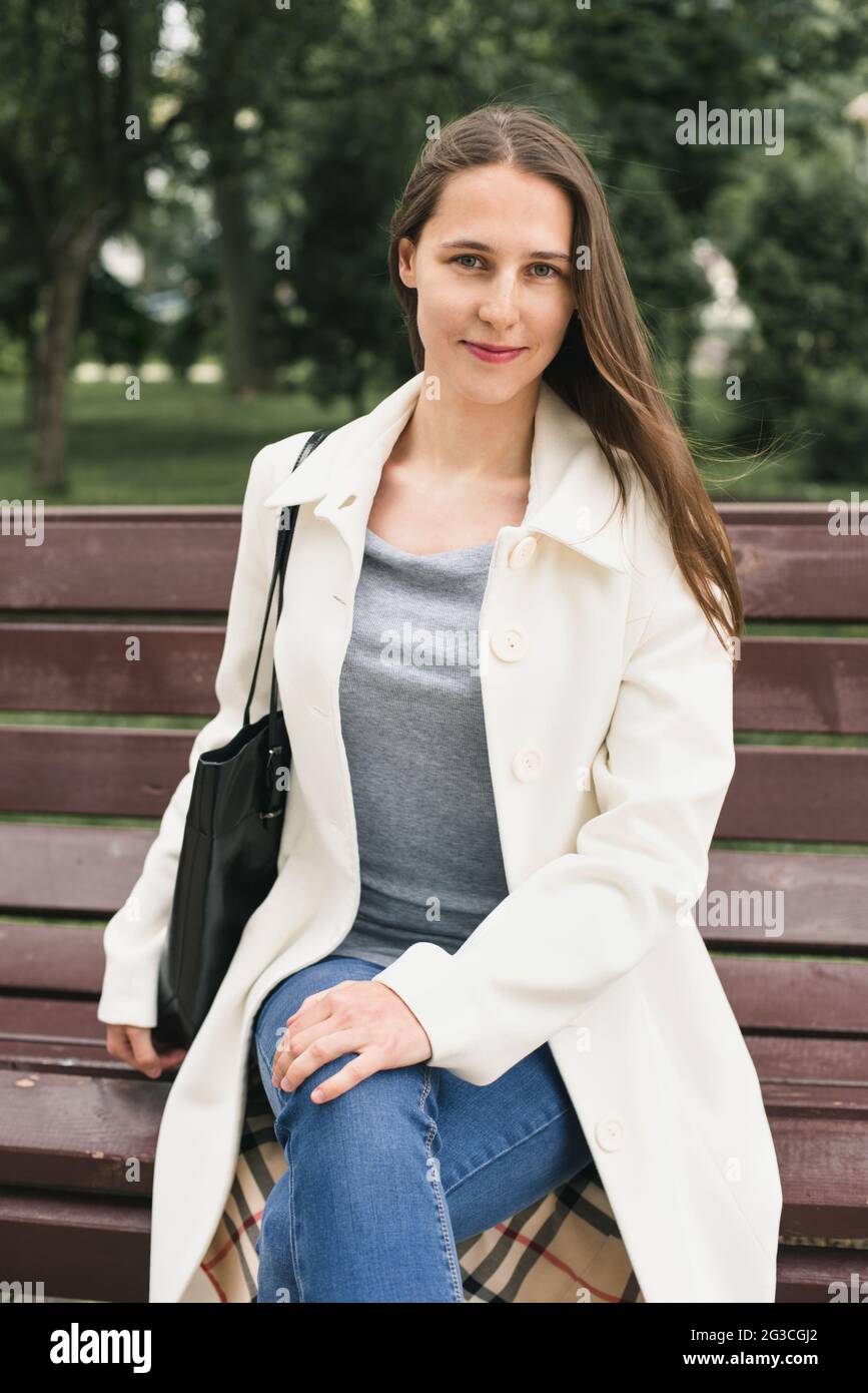 La belle jeune femme de ville est assise sur un banc souriant Banque D'Images